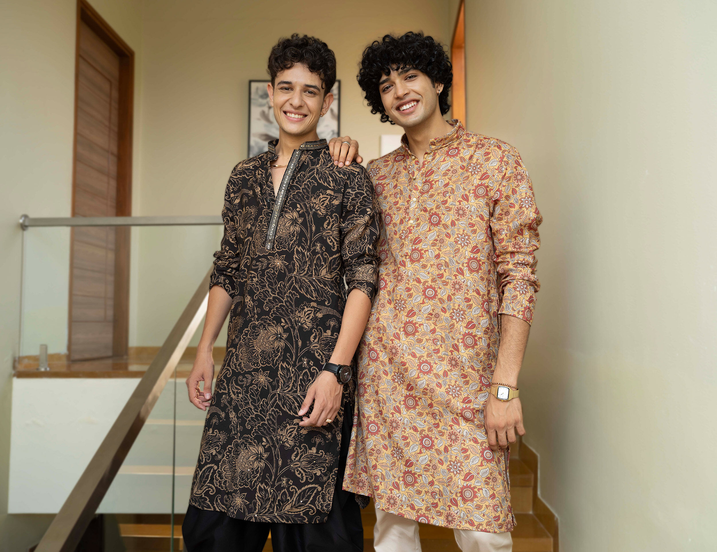 Two men wearing printed kurtas in contrasting floral and geometric patterns showcase contemporary ethnic fashion with relaxed festive styling.